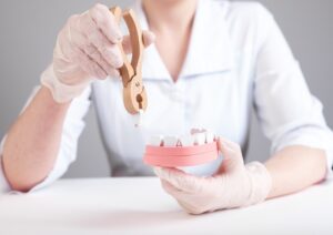 Dentist pulling tooth with forceps out of jaw model. Wisdom teeth extraction or poor oral hygiene, injury consequences. Dental surgeon in lab coat and gloves sitting at table.